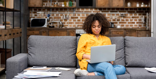 A woman sitting on a couch holds a laptop.