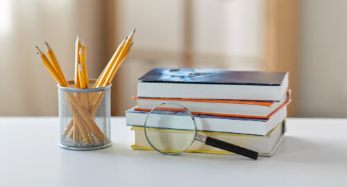 Pencils in a cup, a stack of books and a magnifying glass.