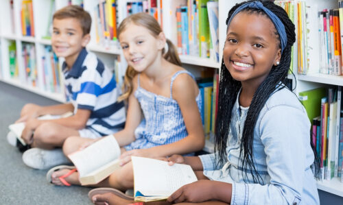 Three young students smiling in a library.