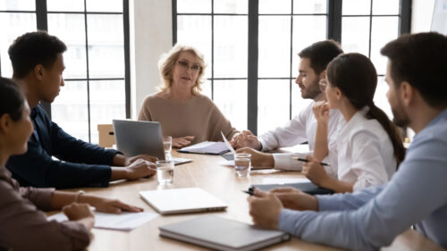 A group of six people sit at a table having a meeting.