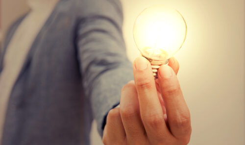 A person holding an illuminated lightbulb.