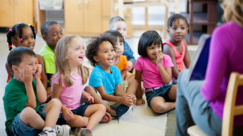 young students sitting in front of a teacher reading them a book