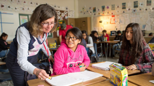 teacher standing next to student at desk